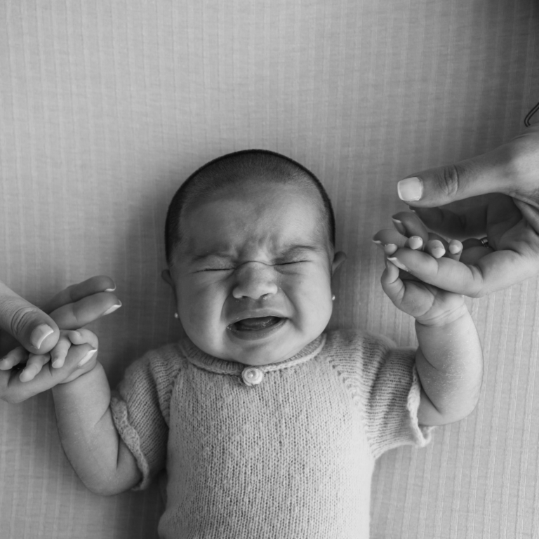 Zwart-witafbeelding van een huilende baby die wordt getroost door twee volwassen handen.